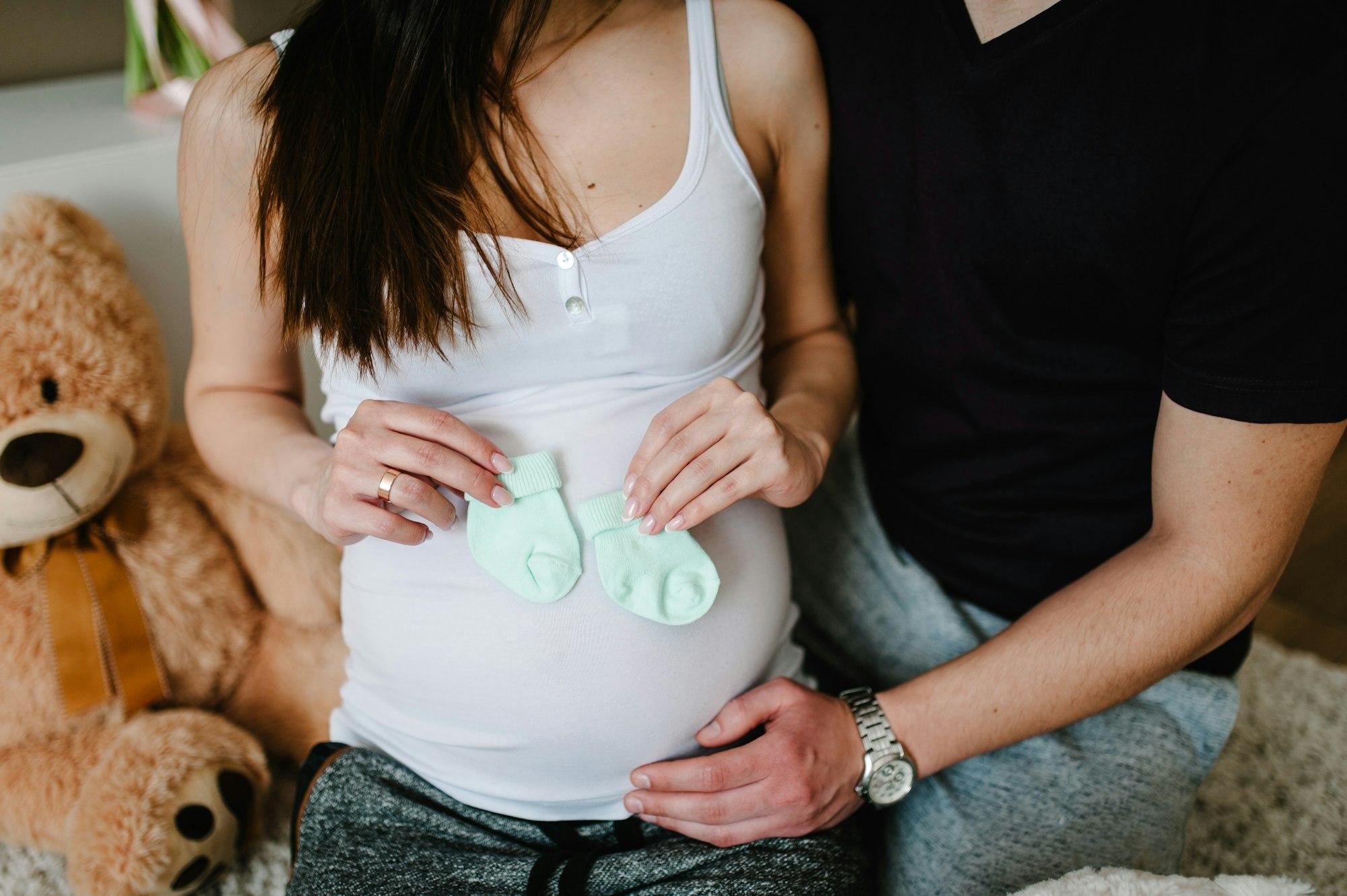 Cropped image of husband holding belly of his pregnant wife, socks for baby in hands. Pregnant woman