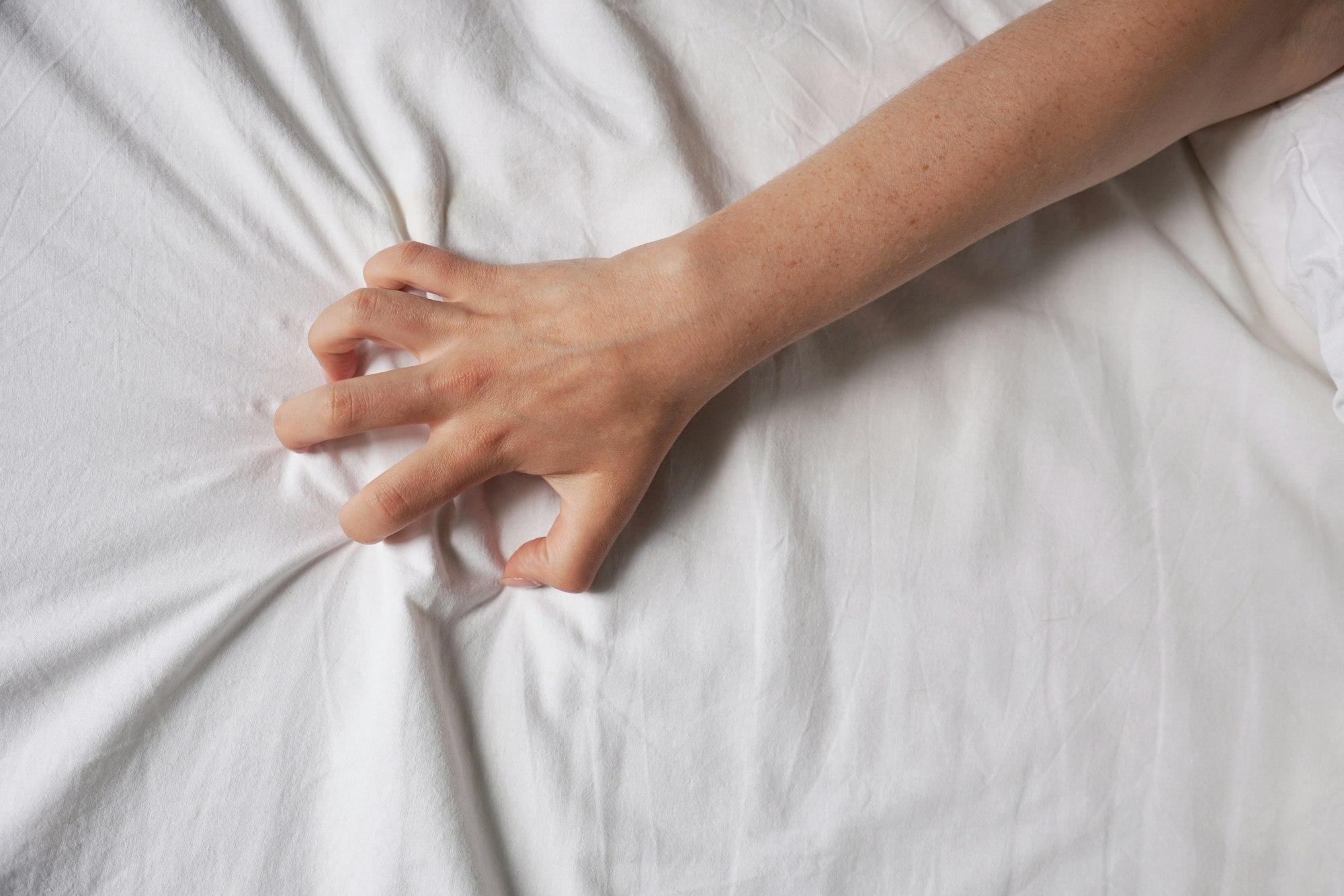 hand of unrecognizable woman grabs bed sheet during sex