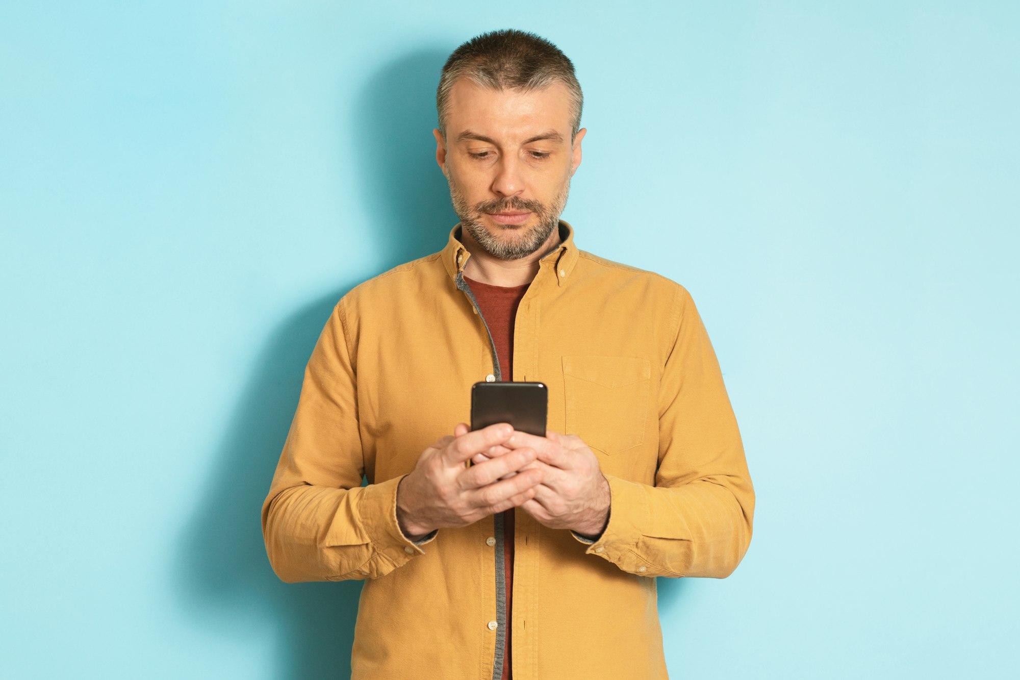 Mature caucasian man using cellphone, texting via smartphone, communicating online standing over