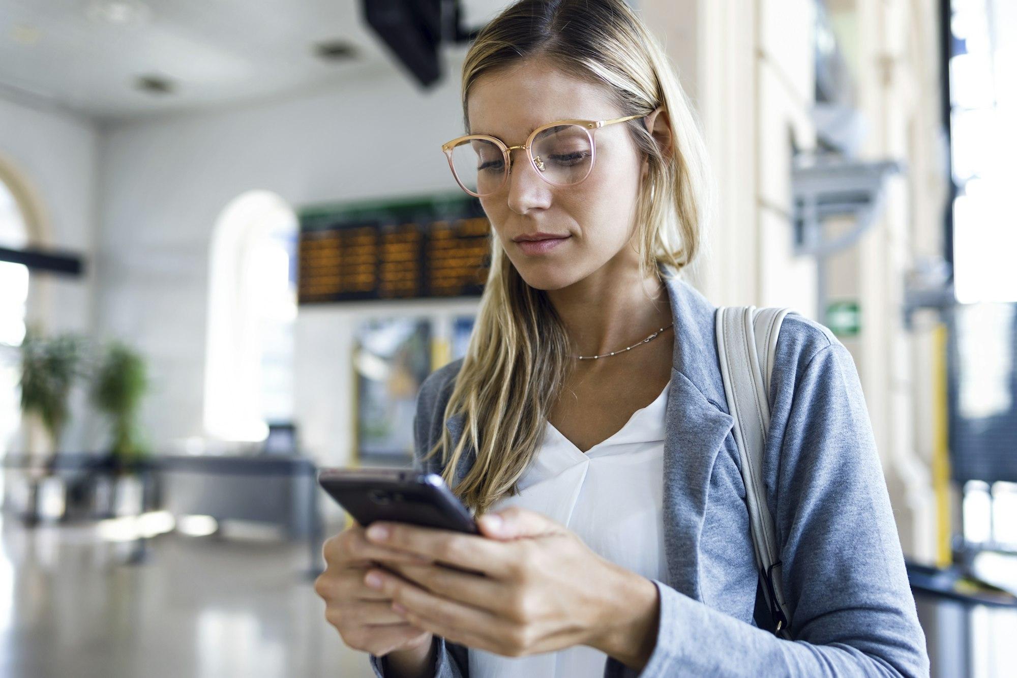 Young woman texting with her mobile phone in the train station hall